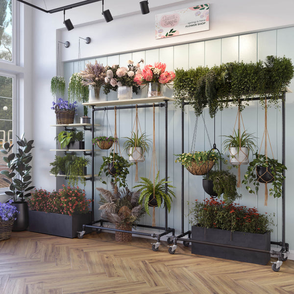 Clothing racks made from dark iron pipes with wheels and a shelf on the top used in a flower store
