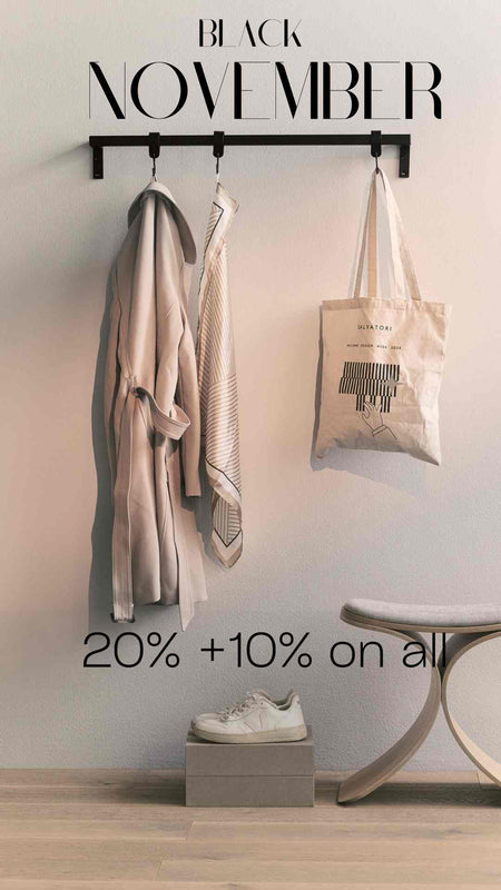 Hellgraue Wand mit schwarzer Garderobe, beiger Mantel, Schal, Stofftasche und weißer Sneaker auf grauem Karton